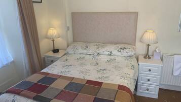 A neatly made bed with floral bedding, two bedside lamps, a small bedside table with a clock, and a radiator.