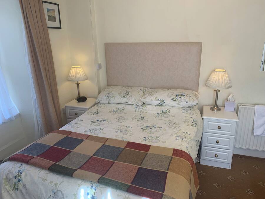 A neatly made bed with floral bedding, two bedside lamps, a small bedside table with a clock, and a radiator.