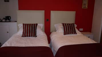 Dos camas individuales con ropa de cama a rayas y almohadas rojas, una mesita de noche pequeña y una pared roja con cuadros enmarcados.