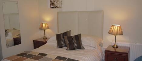 A neatly made bed with a checkered bedspread, two bedside lamps, a mirror, and a wall-mounted artwork.