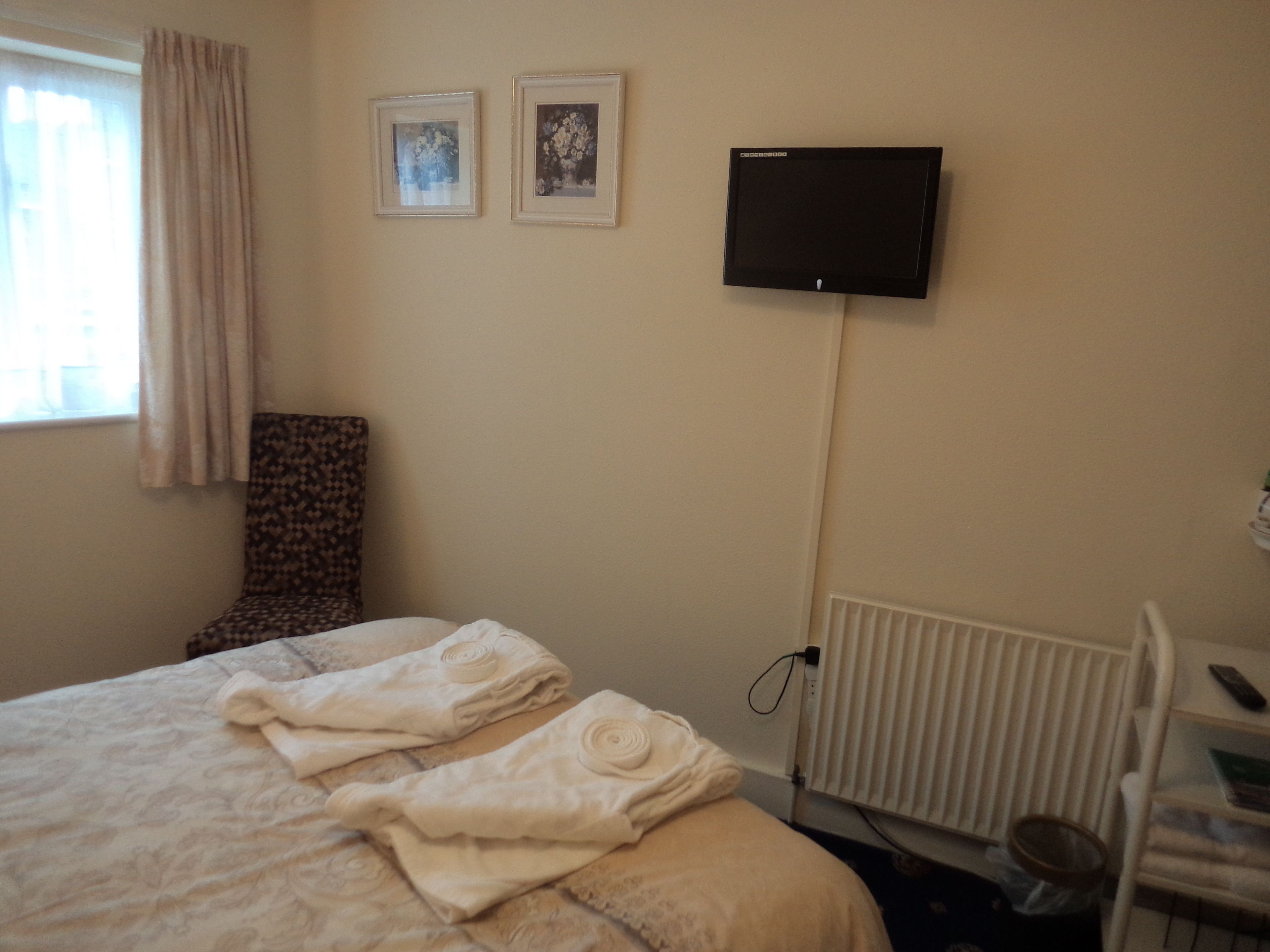 A hotel room with a bed, a chair, a television mounted on the wall, and a window with curtains.