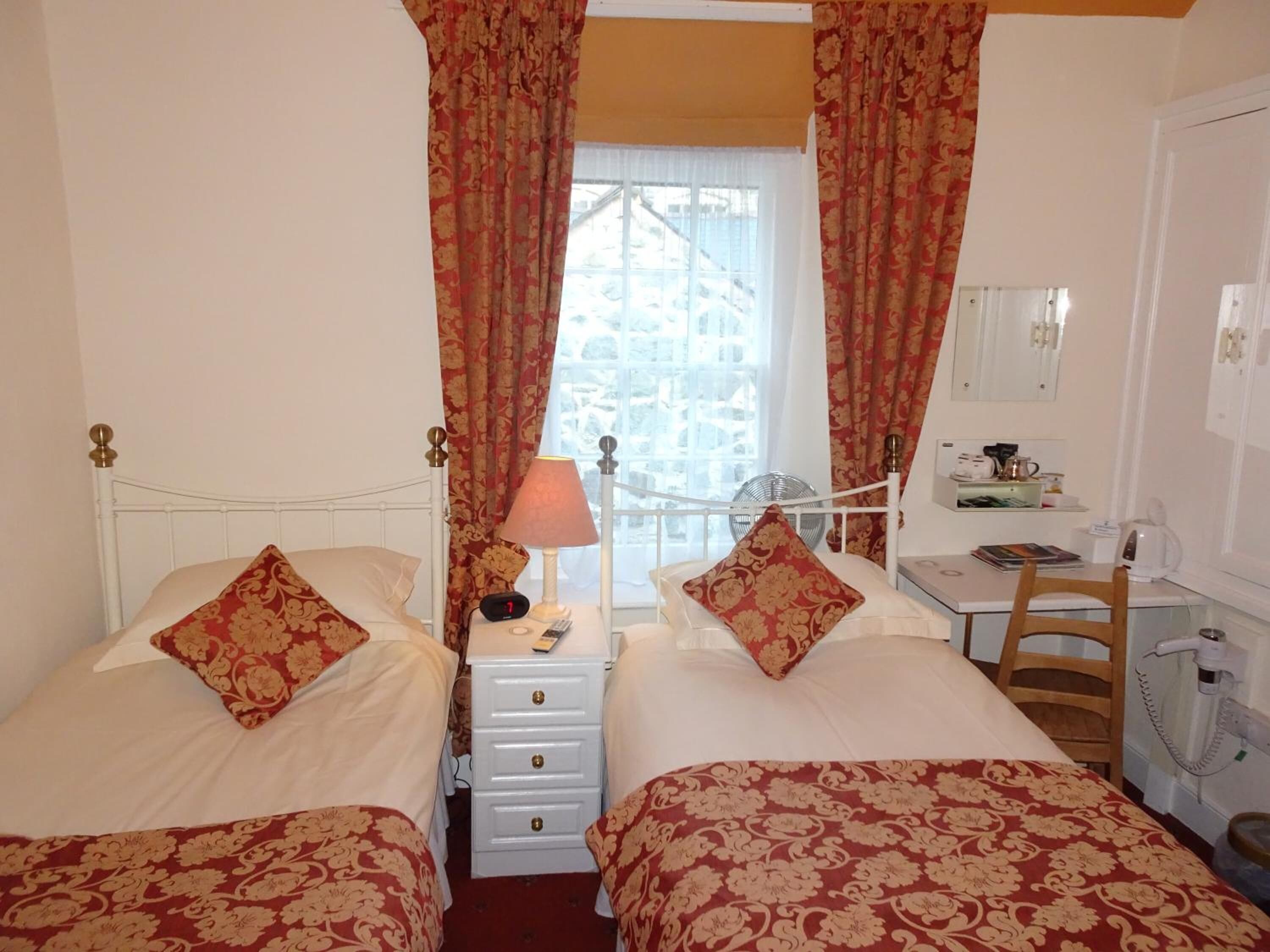 A hotel room with two beds, a desk, a chair, a lamp, and a window with curtains.