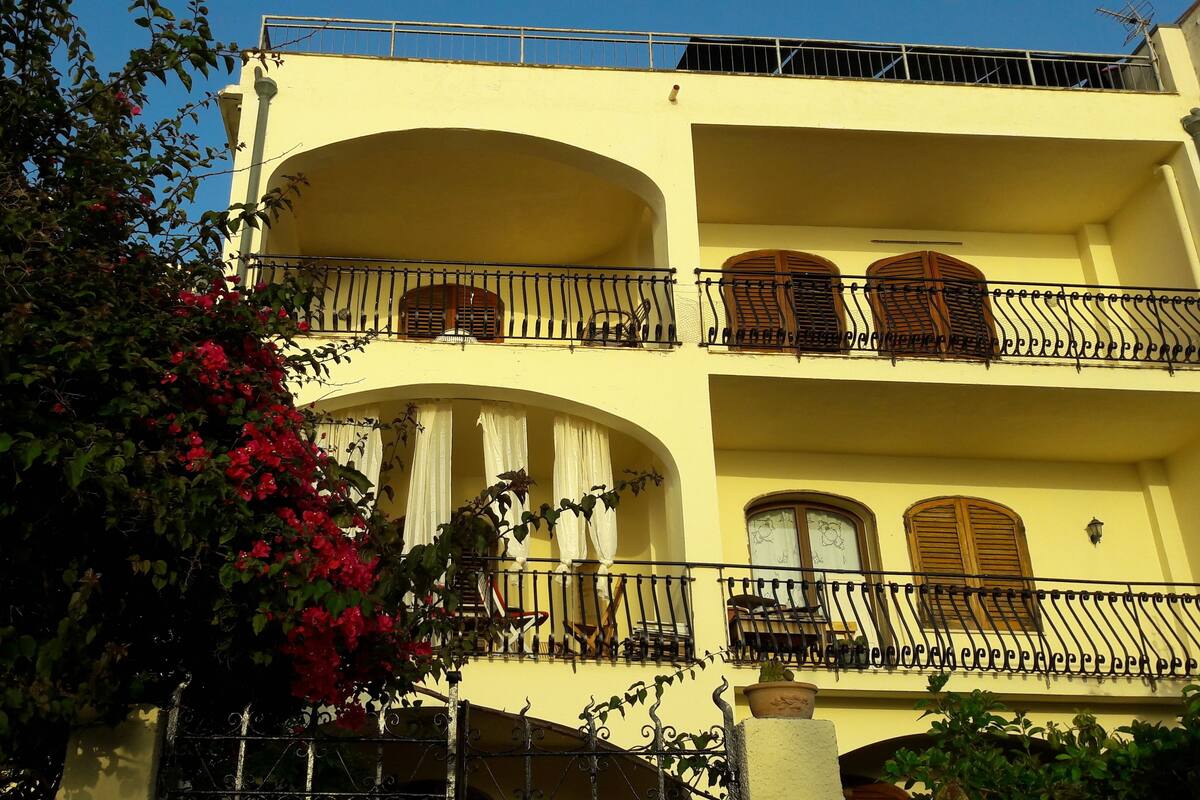 Um edifício de vários andares com varandas, janelas em arco e fachada amarela.