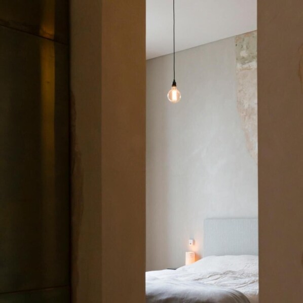 A bedroom with a single bed, a nightstand, and a hanging light fixture.