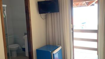 A room with a television mounted on the wall, a blue refrigerator, a bathroom with a toilet and sink, and a door leading outside.