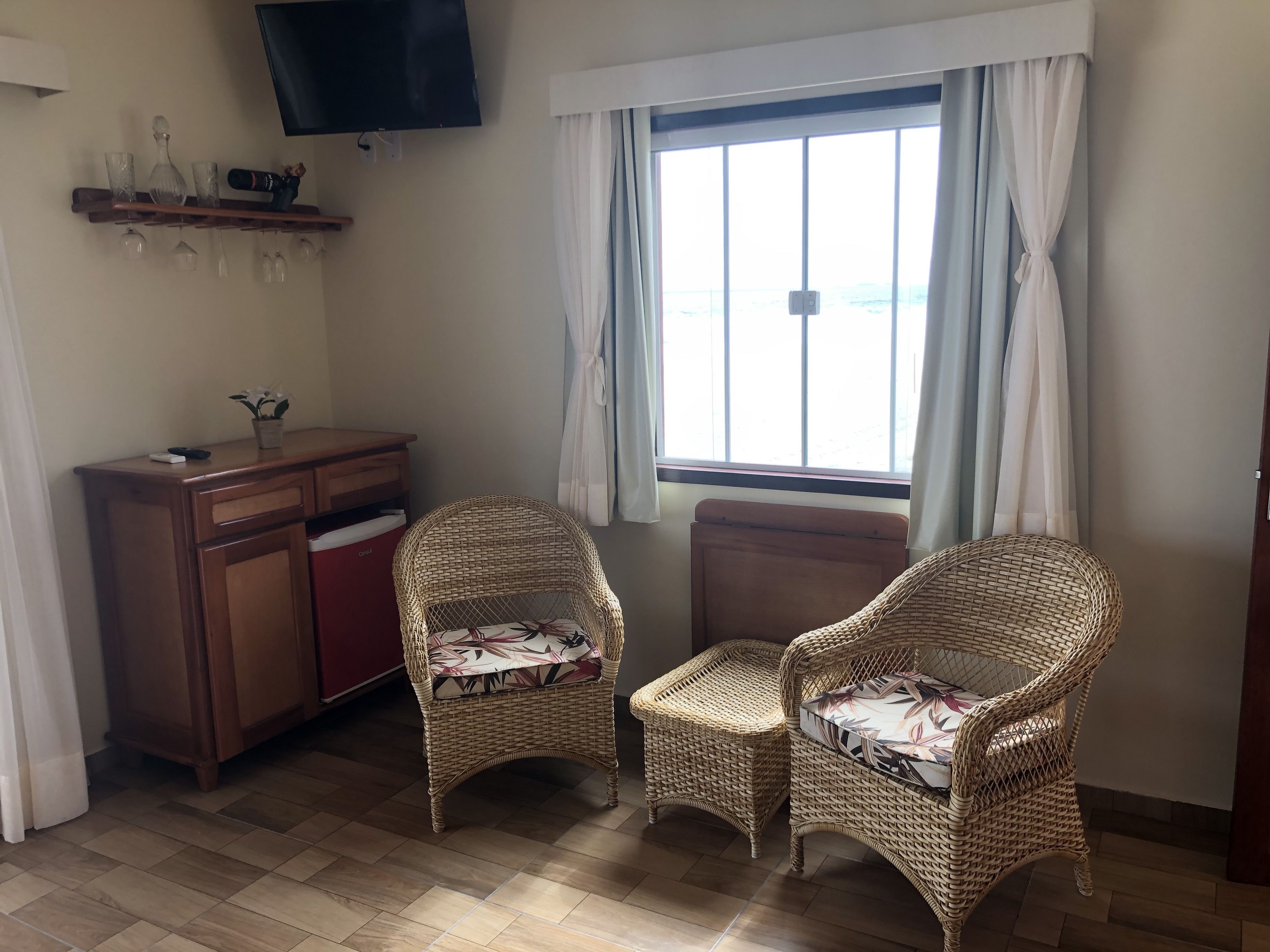 Ein Zimmer mit zwei Korbstühlen, einem Holzschrank, einem Fernseher und einem Fenster mit Vorhängen.
