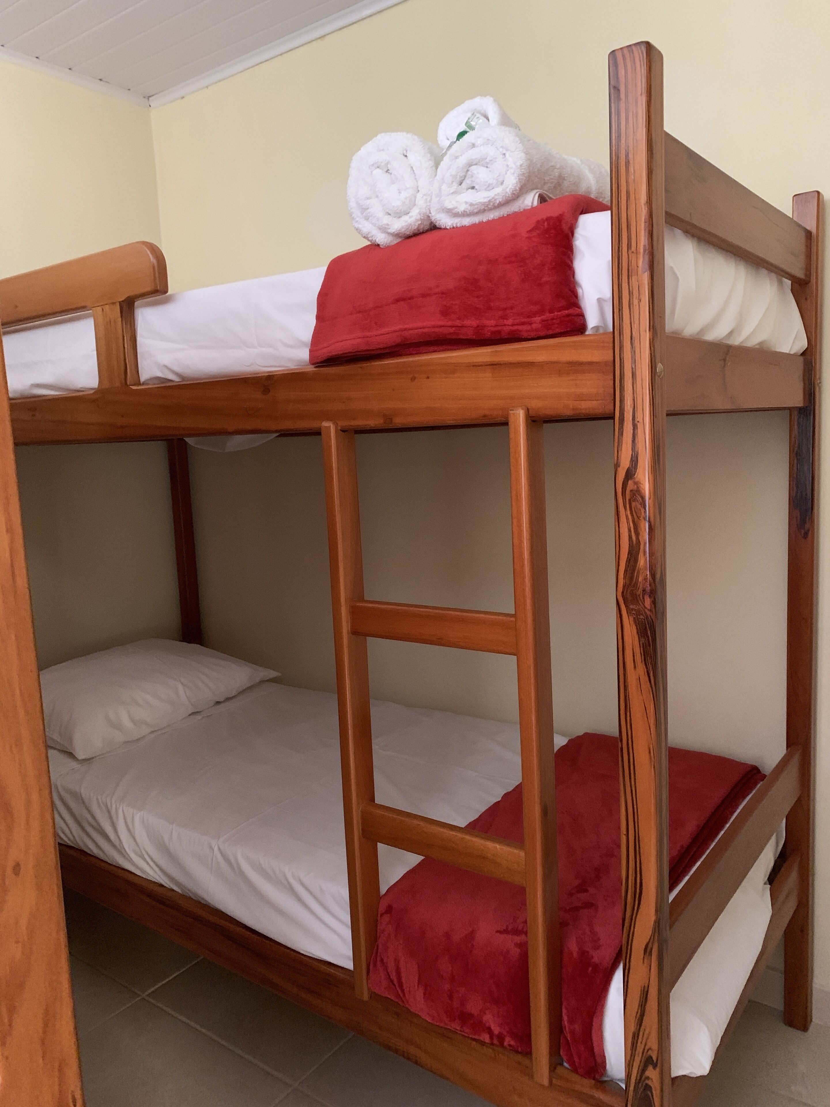 A bunk bed with white and red bedding, a wooden headboard, and a red blanket on the top bunk.