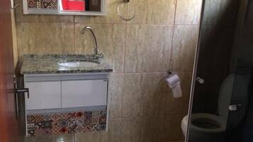 A bathroom with a tiled floor, a sink with a faucet, a toilet, and a shower area with a glass door.