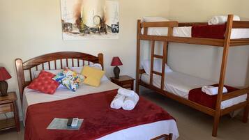 Una habitación con una cama individual, una cama litera, una manta roja, una lámpara y un cuadro en la pared.