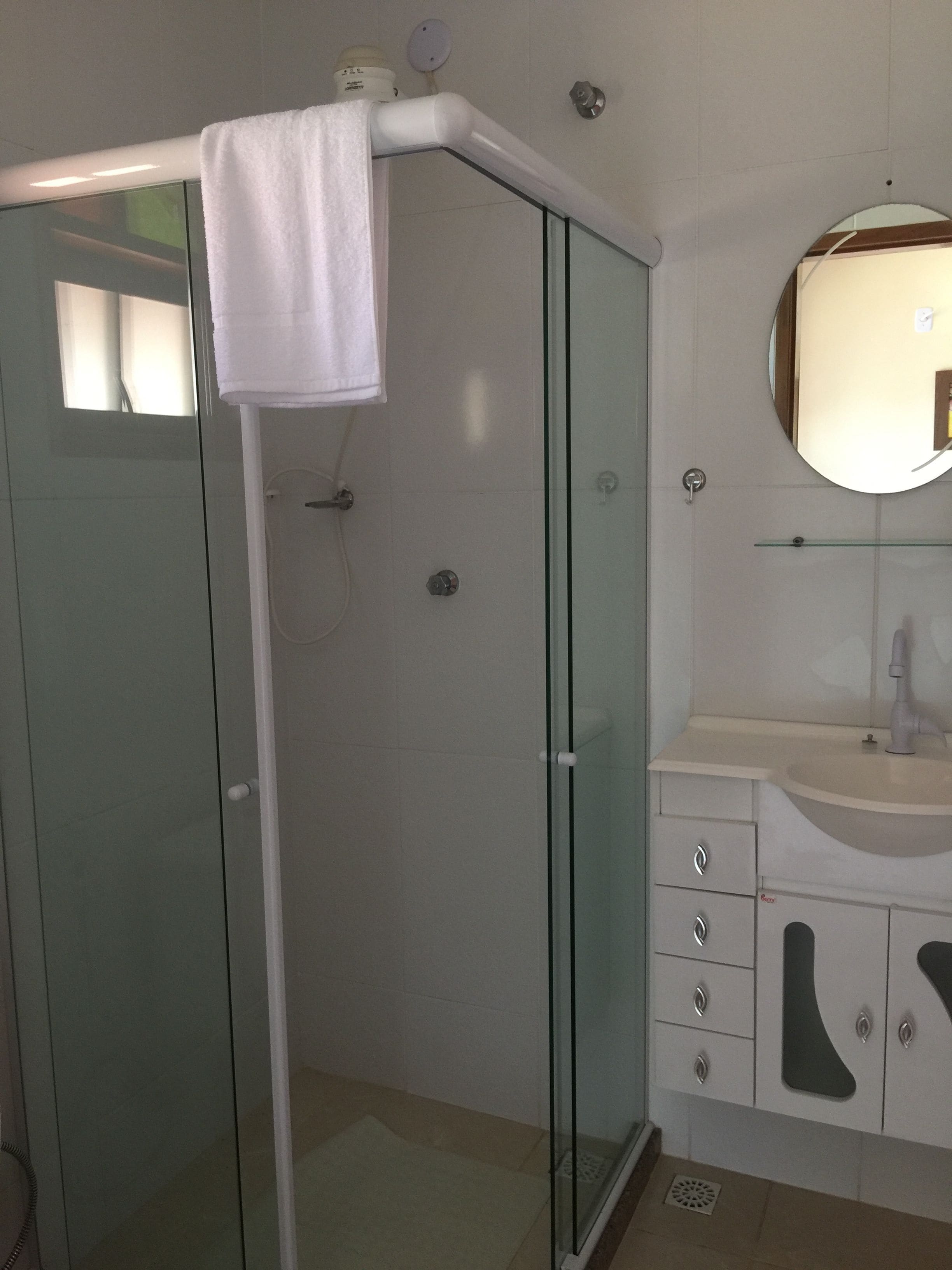 Un baño moderno con cabina de ducha de vidrio, un lavabo blanco y un mueble de tocador con cajones.