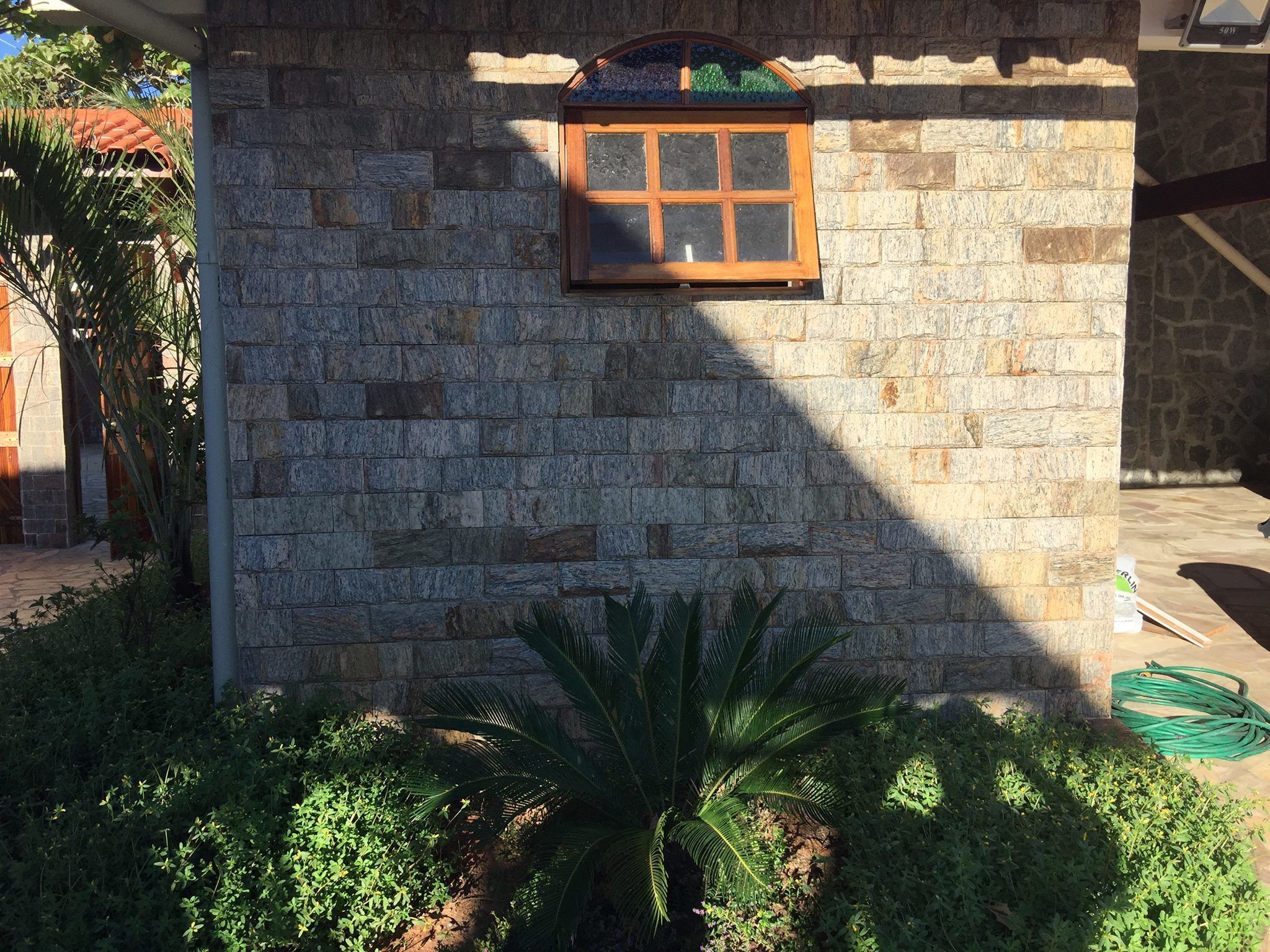 A stone wall with a window and a palm tree in front.