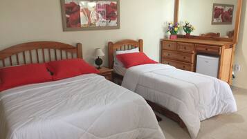 Habitación de hotel con dos camas, cada una con ropa blanca y almohadas rojas, un cabecero de madera, una mesita de noche con lámpara, un aparador y un espejo.