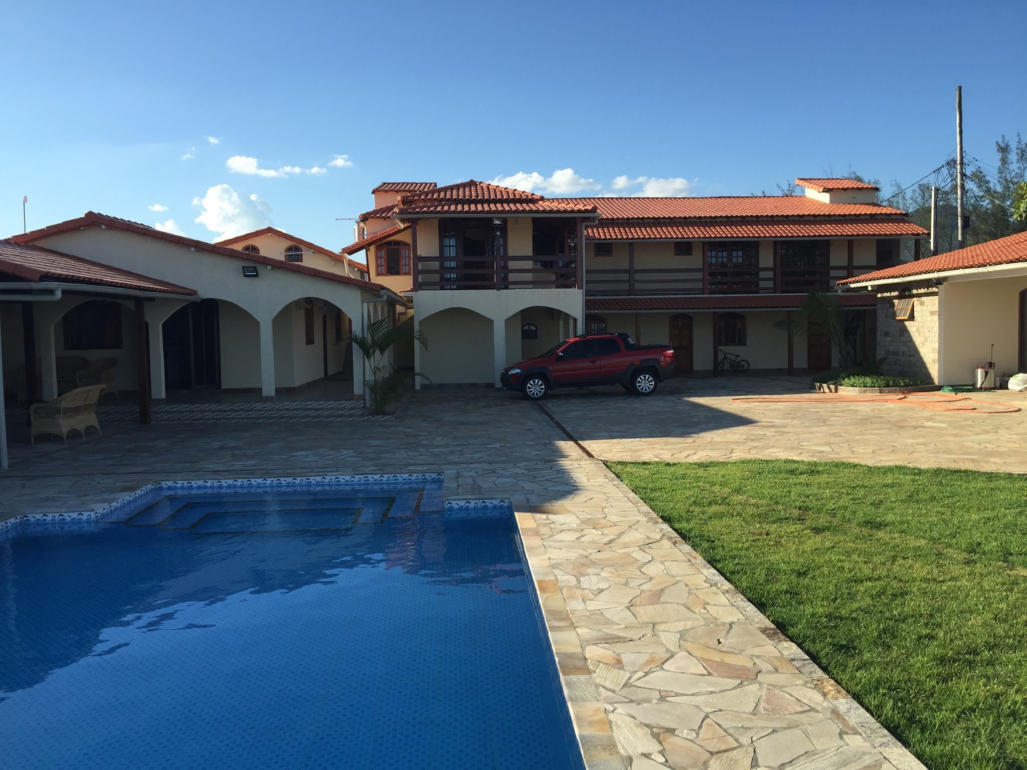Una casa de dos pisos con piscina, un automóvil rojo estacionado en la entrada y un césped bien cuidado.
