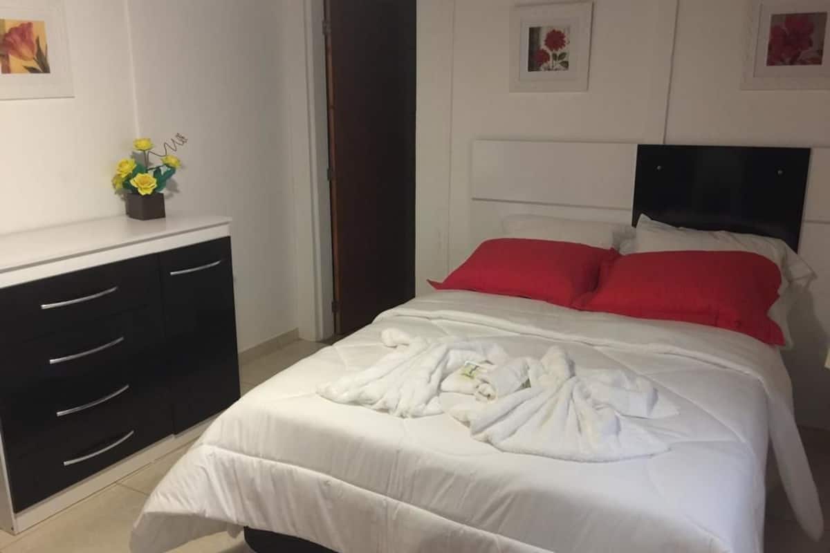 Quarto de hotel com cama, penteadeira e uma mesinha com um vaso de flores.