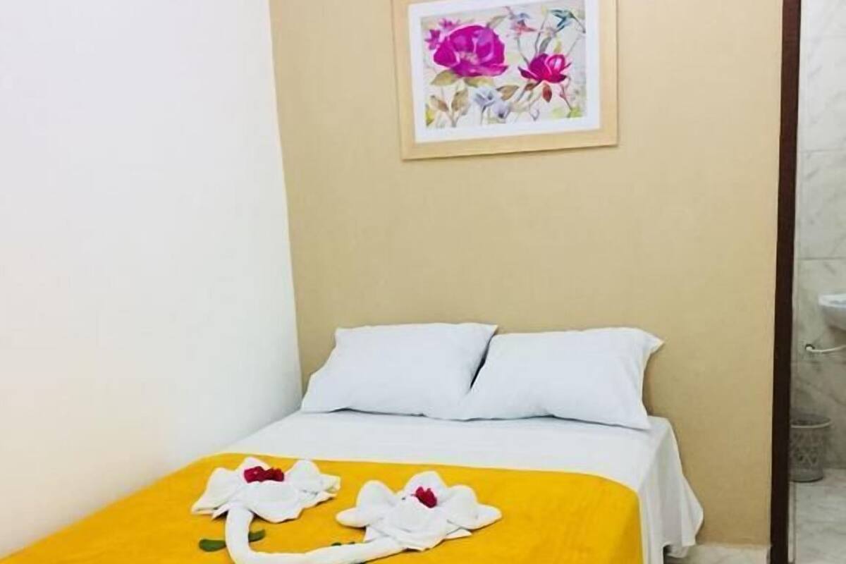A hotel room with a bed, a yellow throw blanket, and a floral artwork on the wall.