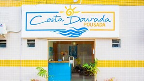A Costa Dourada Pousada with a blue and yellow facade, potted plants, and a visible interior with a bed and a painting. - Pousada Costa Dourada (Ipojuca)