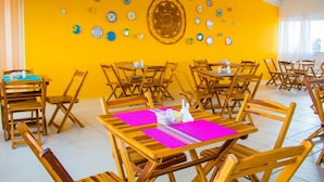 A dining area with wooden tables and chairs, a bright yellow wall with decorative plates, and a large window providing natural light. - Pousada Costa Dourada (Ipojuca)