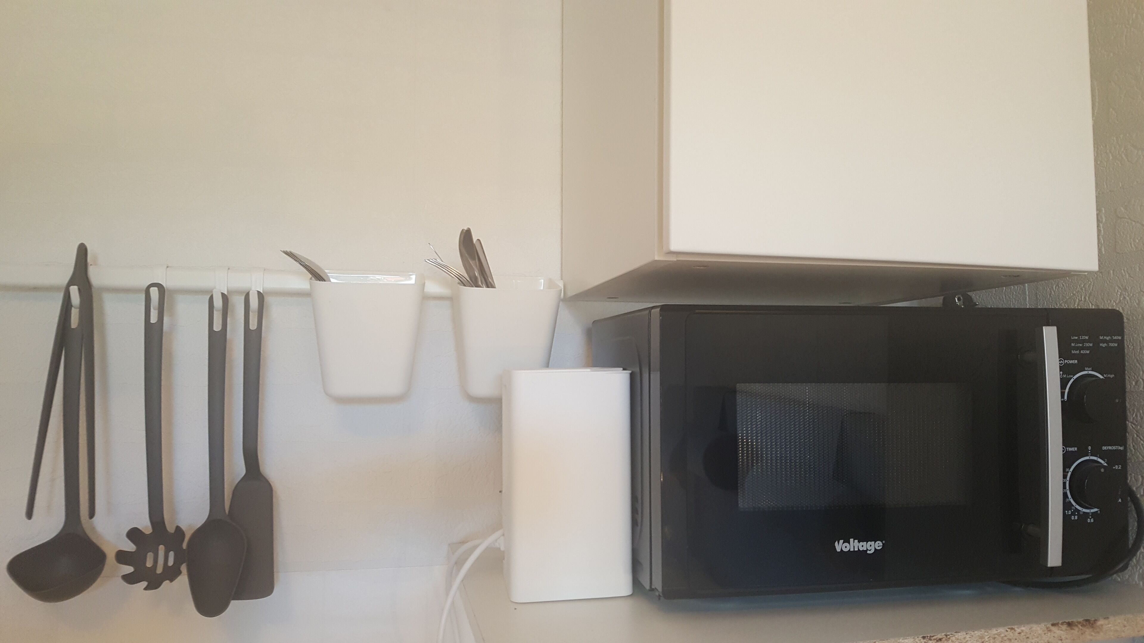 A kitchen with a microwave, utensils, and a white appliance.