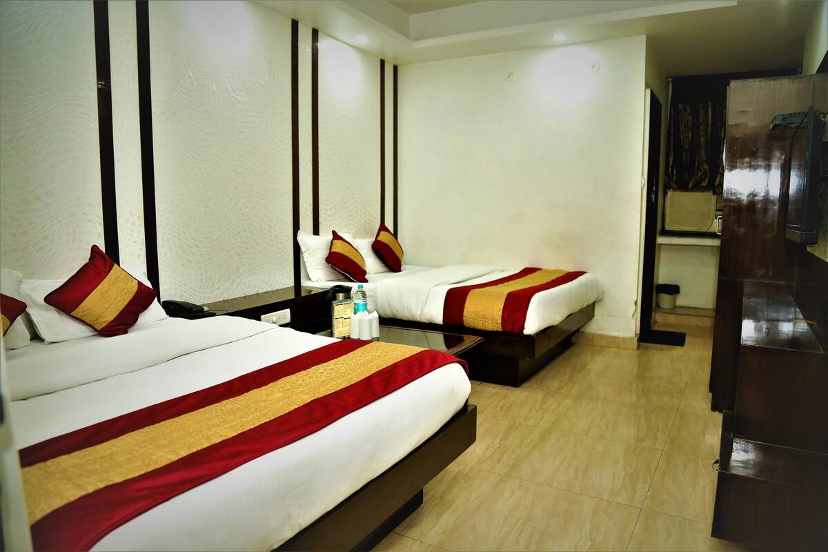Habitación de hotel con dos camas, cada una con cubrecamas a rayas rojas y doradas, almohadas blancas y una mesita con artículos de tocador.