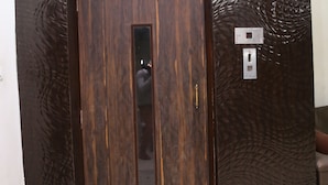 A wooden door with a vertical mirror and a light switch on a textured wall. - Hotel Suzi International (New Delhi)