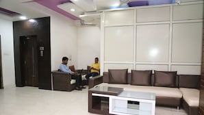 A modern waiting area with a sofa, a glass coffee table, and a dark wooden door. - Hotel Suzi International (New Delhi)