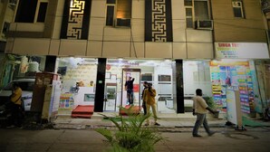 A multi-story hotel with illuminated vertical patterns on the facade, a ground-level entrance with a ticket counter, and a signboard for a travel agency. - Hotel Suzi International (New Delhi)