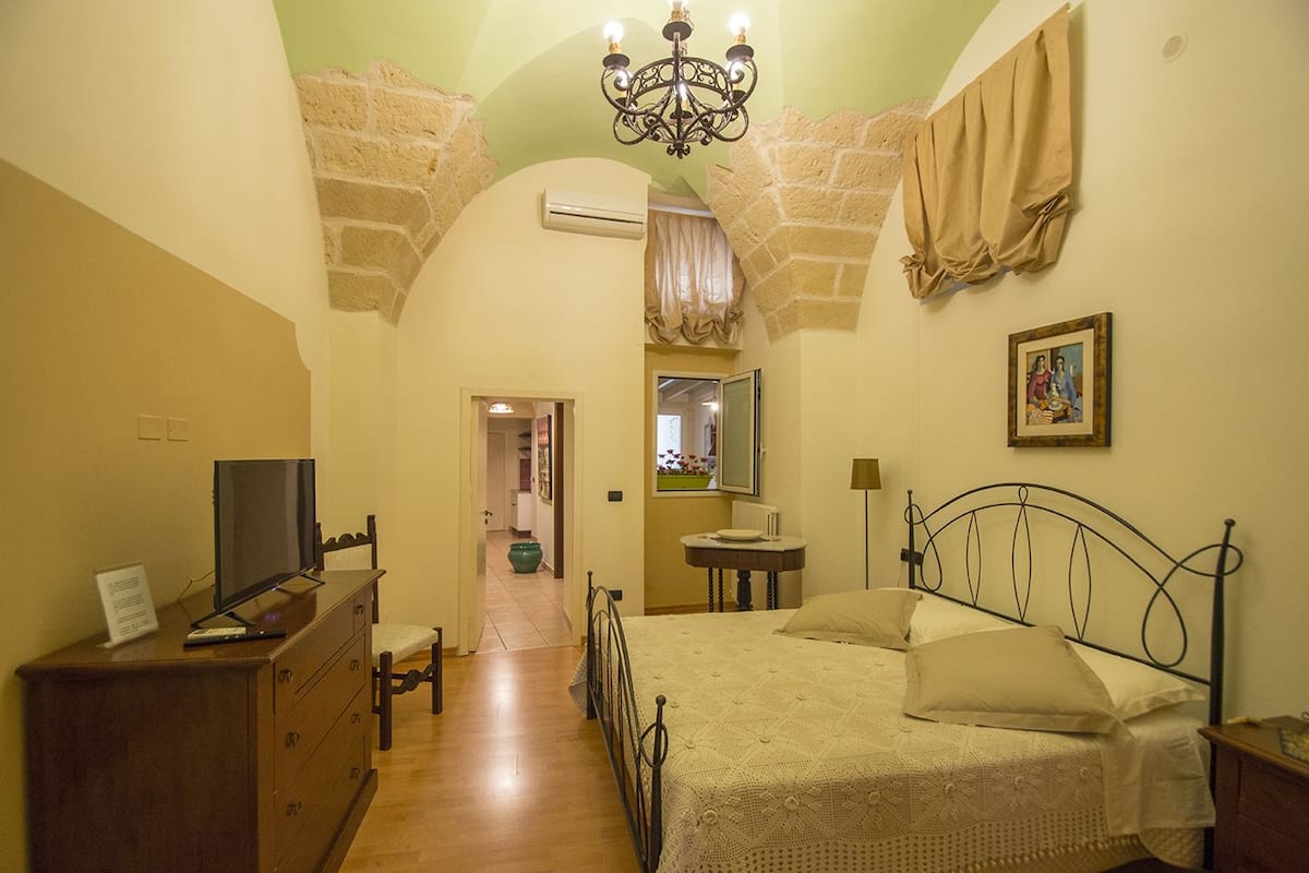 A bedroom with a bed, a dresser, a television, a mirror, and a chandelier.