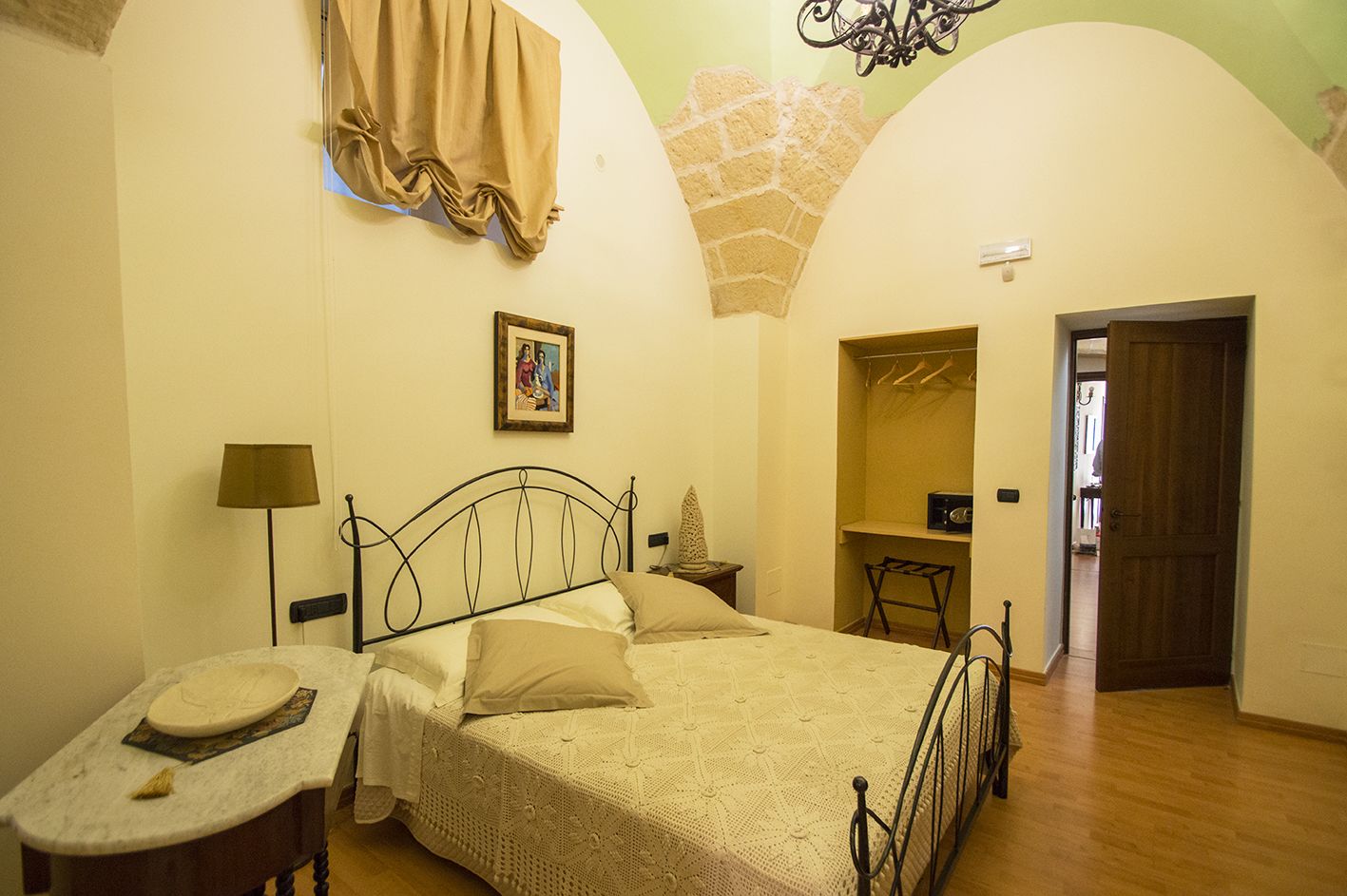 Une chambre à coucher comprenant un lit, une table de chevet, une lampe, un tableau accroché au mur, une armoire et une porte donnant sur une autre pièce.