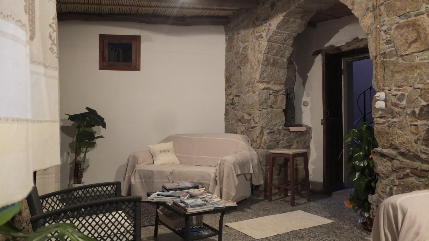 Una sala de estar acogedora con una pared de piedra, un sofá, una mesita de centro con revistas y un taburete pequeño.