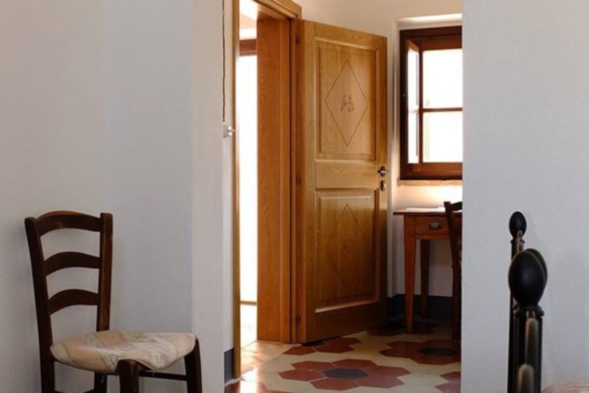 A wooden chair in a hallway with a door and a small table with a lamp.