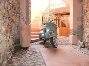 A vintage Vespa parked in a stone-walled courtyard with a tiled floor and a wooden door in the background. - Casa Camilla (San Vito)
