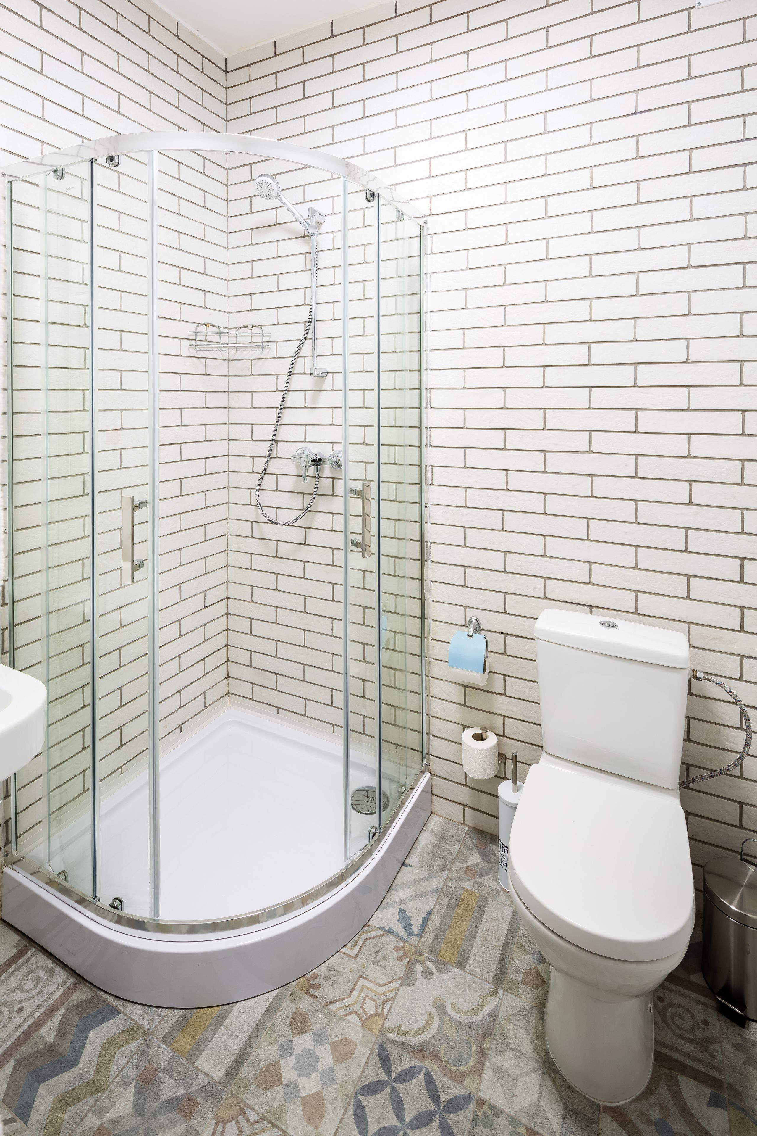 Un baño con cabina de ducha de vidrio, un inodoro y baldosas de suelo con diseño.