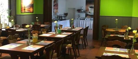 A restaurant with green walls, wooden tables, and chairs. There are flower vases on the tables.