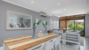 A modern dining area with a wooden table, white chairs, and a large mirror. - San Lameer Villa Rentals 2537 (Southbroom)