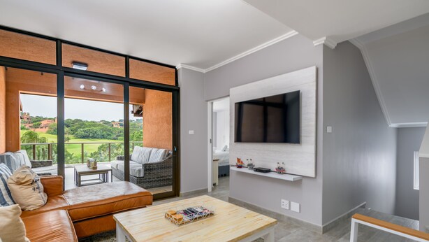 A modern living room with a large TV, comfortable seating, and a view of the outdoors. - San Lameer Villa Rentals 2537 (Southbroom)