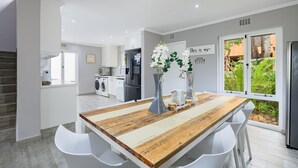 A modern kitchen with white cabinetry, a wooden island with white bar stools, and a view of a lush garden through large windows. - San Lameer Villa Rentals 2537 (Southbroom)