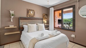 Quarto de hotel com cama grande, ventoinha no teto, obras de arte nas paredes e varanda com mobiliário exterior.