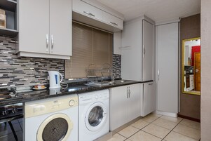 A compact kitchen with a washing machine, a coffee maker, and a sink.