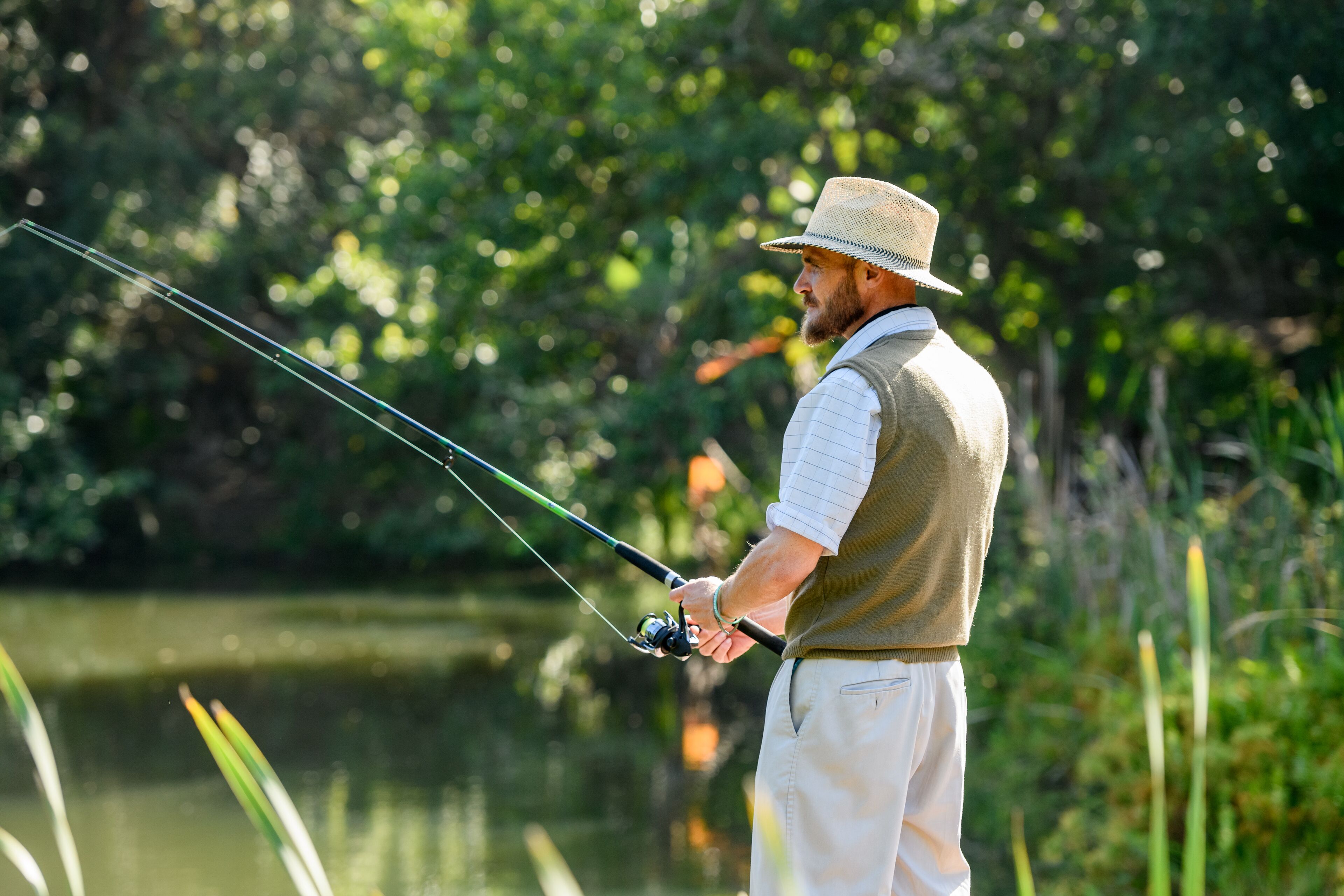 A man fishing by a calm river surrounded by greenery.