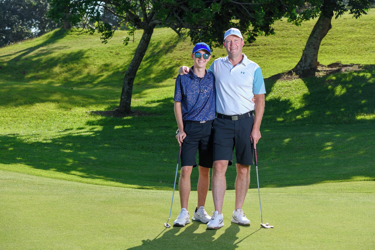 Two people standing on a golf course with trees in the background.