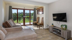 A living room with a sofa, chairs, a TV, and a sliding glass door to a balcony. - San Lameer Villa Rentals One Bedroom Standard 10417 (Southbroom)