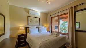 A hotel room with a large bed, a nightstand, a lamp, and a window with curtains. - San Lameer Villa Rentals One Bedroom Standard 10425 (Southbroom)