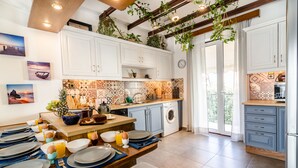 A modern kitchen with white cabinets, a tiled backsplash, and a dining area set up for breakfast. - Casa Ithomi (Chania)