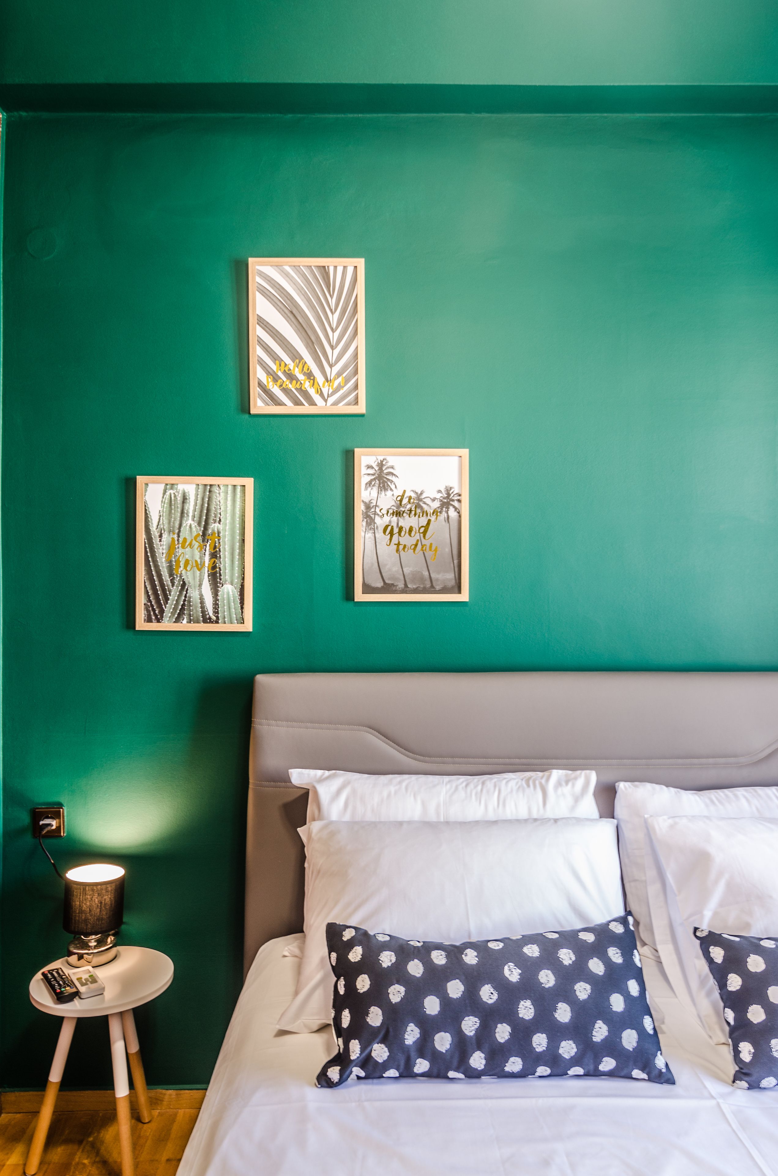 A bedroom with a teal wall, a bed with white bedding and polka dot pillows, and three framed artworks.