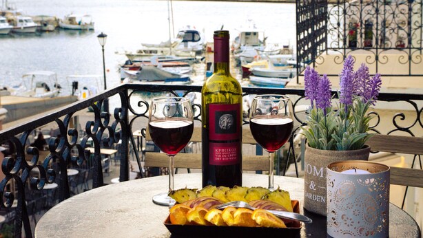 A table with a bottle of wine, two glasses of red wine, a plate of fruit, and a candle holder. - Casa Ithomi (Chania)