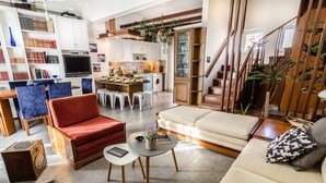 A spacious living area with a red armchair, beige sofa, and a small coffee table. A kitchen with white cabinets and a dining area with a blue chair are visible. - Casa Ithomi (Chania)
