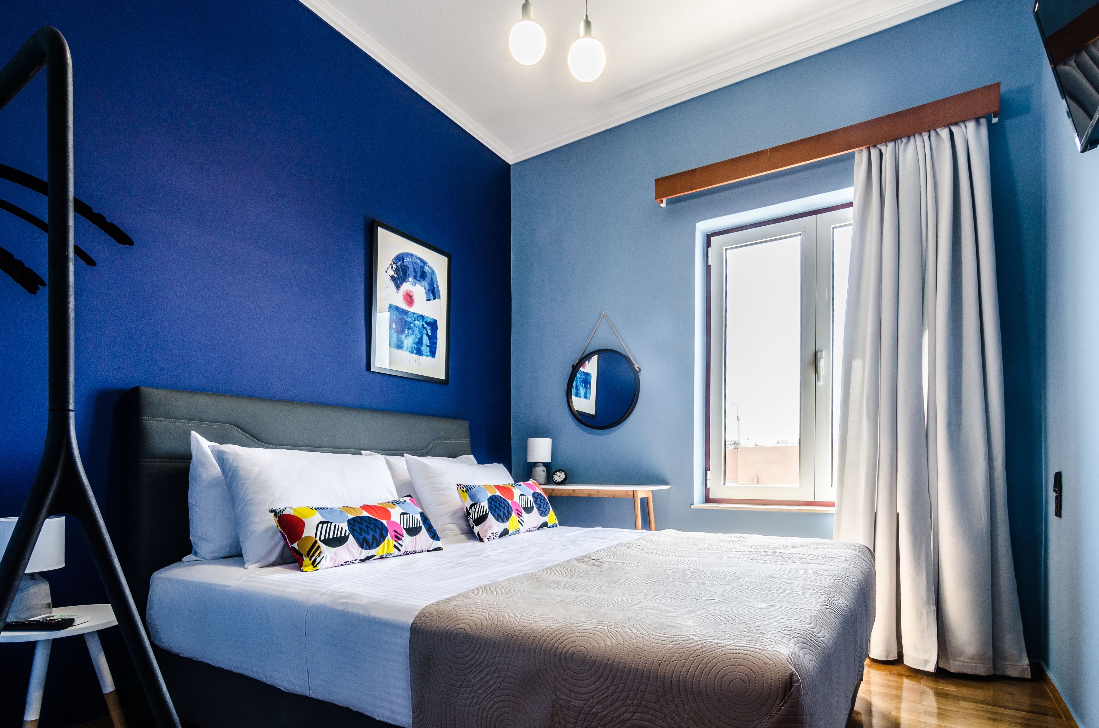 A bedroom with a bed, a bedside table, a lamp, a window with curtains, and a wall with a picture.