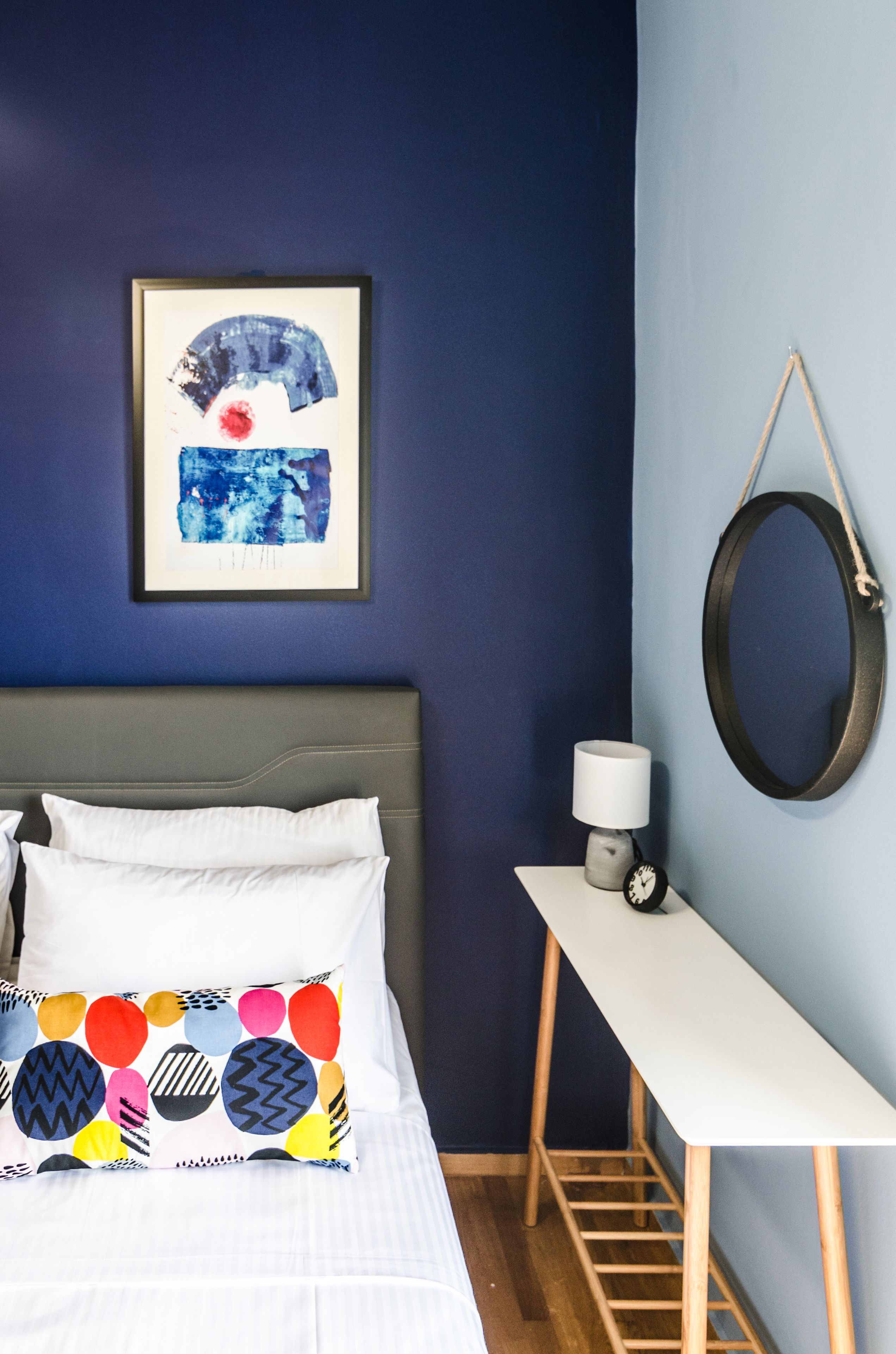 Une chambre à coucher avec un lit, des oreillers, une table de chevet avec une lampe, un tableau encadré et un miroir sur le mur.
