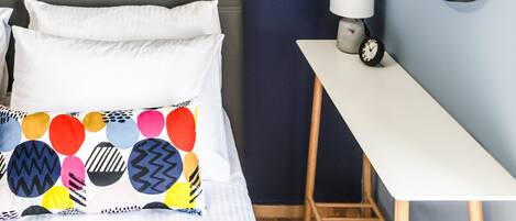 Une chambre à coucher avec un lit, des oreillers, une table de chevet avec une lampe, un tableau encadré et un miroir sur le mur.