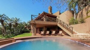 Un espace aménagé au bord de la piscine, comprenant une piscine, des chaises longues et un bâtiment doté d’un balcon.